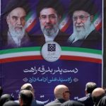 People sit before a banner depicting Iran’s supreme leaders since 1979. (AFP)