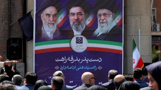 People sit before a banner depicting Iran’s supreme leaders since 1979. (AFP)